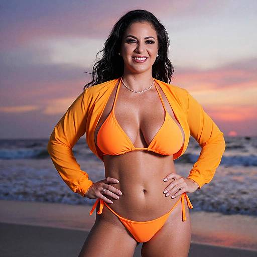 Photograph of a smiling, curvy woman with long dark hair, wearing an orange bikini and open jacket, standing on a beach at sunset.