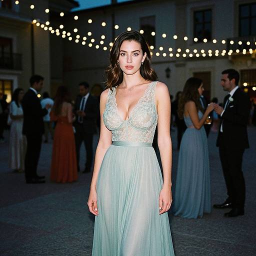 Photograph of a beautiful woman with fair skin and dark hair in a low-cut, white lace and chiffon gown, standing in an outdoor evening event