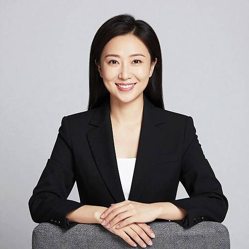 Photograph of an Asian woman with long black hair, smiling, wearing a black blazer over a white top, seated against a white background.