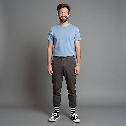 Photograph of a bearded man with short dark hair, wearing a light blue T-shirt, black pants, and black-and-white striped socks with black