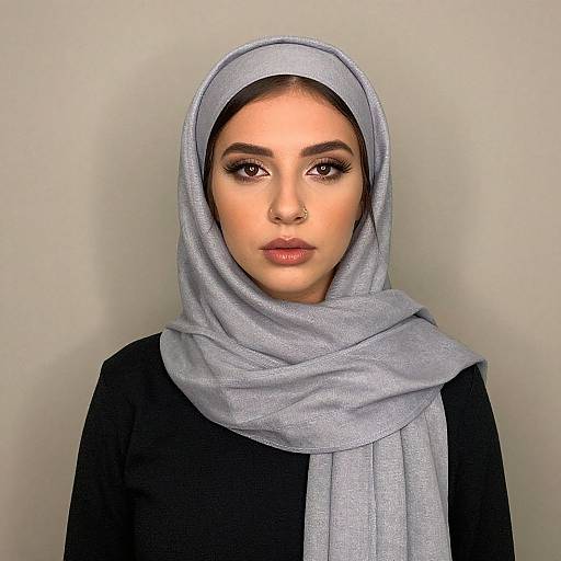 Photograph of a young woman with medium skin tone, dark eyebrows, and brown eyes, wearing a light gray hijab and black top, against a