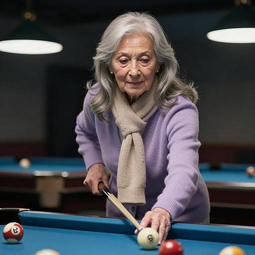 Elderly woman with gray hair, wearing purple sweater and beige scarf, aims cue stick at pool ball in dimly lit billiards room.
