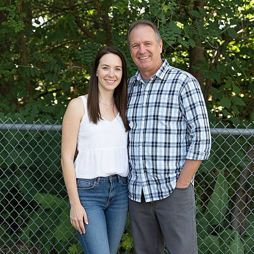 Photograph of a smiling Caucasian couple standing outdoors; woman in white tank top and blue jeans, man in plaid shirt and gray pants, in front