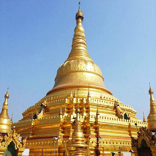 Photograph of a golden Buddhist stupa with a tall, spiraled spire, set against a clear blue sky. Detailed, ornate architecture with