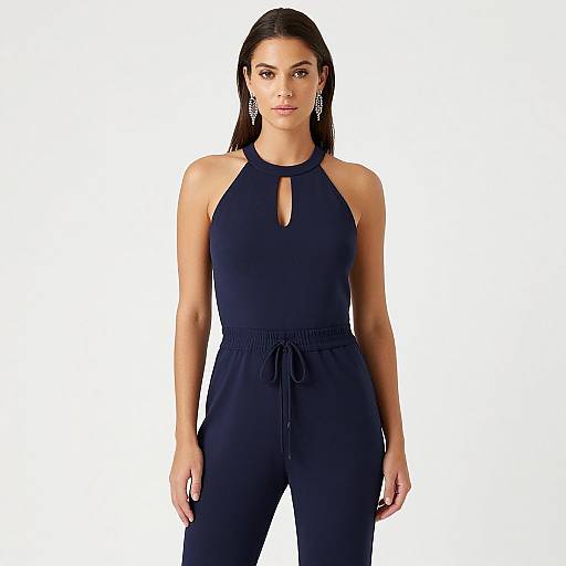 Photograph of a confident woman with long dark hair, wearing a sleeveless, black halter-neck jumpsuit with a keyhole cutout, and