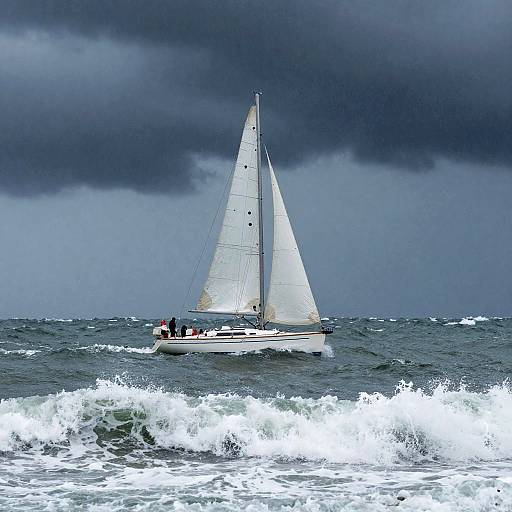 Photograph of a white sailboat with two people on board navigating choppy ocean waves under a dark, stormy sky.