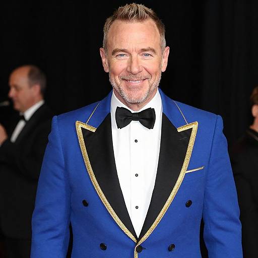 Photograph of a smiling middle-aged man with short gray hair and beard, wearing a blue tuxedo with black and gold trim, white shirt,