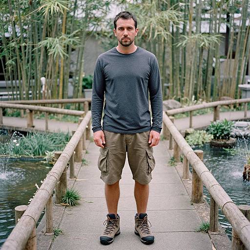 Photograph of a bearded man with short dark hair, wearing a dark long-sleeve shirt, khaki cargo shorts, and brown hiking boots