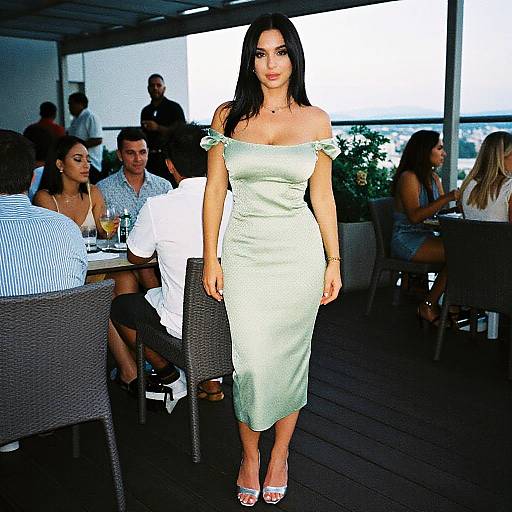 Photograph of a woman with long black hair, wearing an off-shoulder, light green, form-fitting dress and white heels, standing on