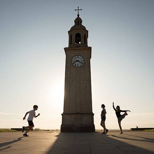 Photograph of three silhouetted dancers in front of a tall clock tower at sunset, with bright sunlight behind and long shadows.