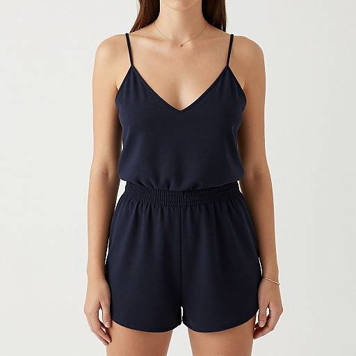 Photograph of a woman wearing a black, spaghetti-strap, V-neck romper with a gathered waist, standing against a white background.
