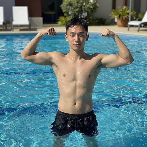 Young Asian man with short black hair, muscular build, flexing arms in a blue pool, wearing black swim trunks, sunny outdoor setting.
