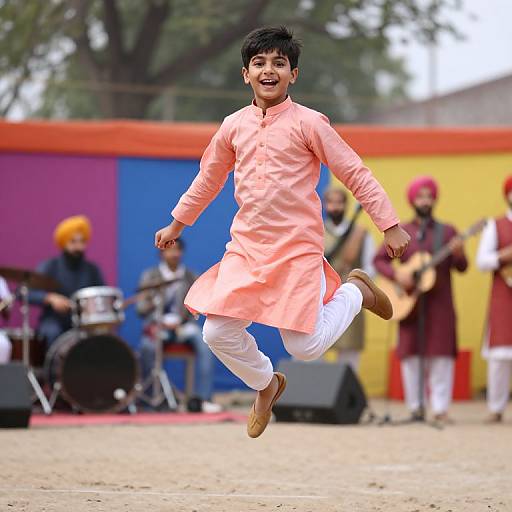 Photograph of a joyful young boy in a pink kurta and white pants, mid-jump, with a colorful background and musicians playing in the background