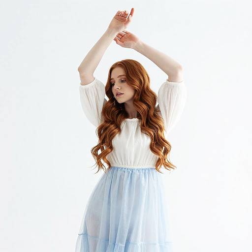 Photograph of a fair-skinned, red-haired woman with long wavy hair, wearing a white blouse and blue tulle skirt, arms raised,