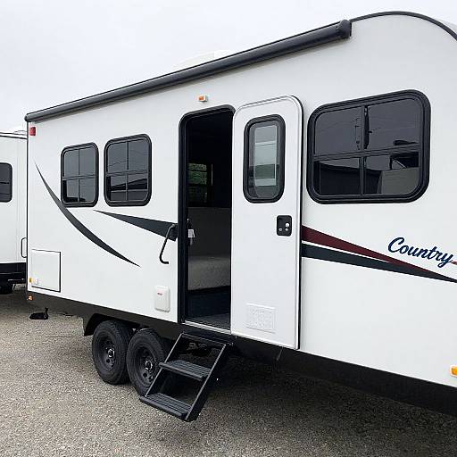 Photograph of a white, single-level, recreational caravan with black trim and a black door, parked on a gravel surface. 
