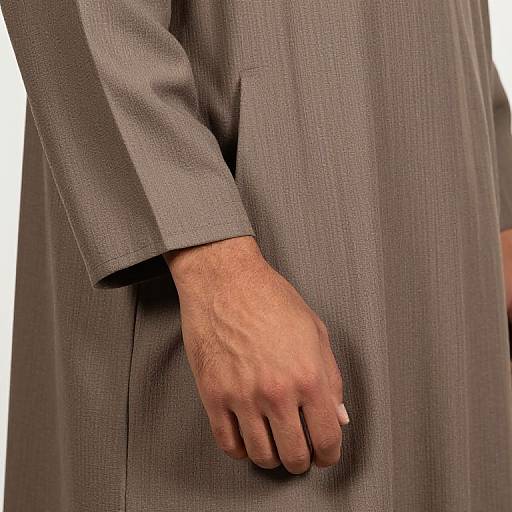 Close-up photograph of a person's right hand in a gray, textured suit sleeve, holding a cigarette, against a plain white background.