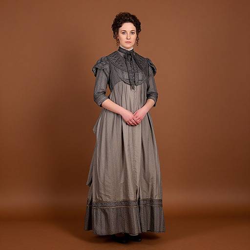 Photograph of a pale-skinned woman with curly dark hair, wearing a Victorian-era grey dress with black lace details, standing against a brown backdrop,