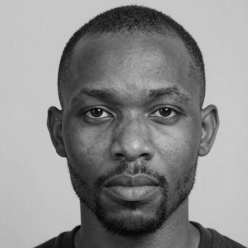 Black and white close-up photograph of a serious-faced African-American man with short hair, beard, and mustache, wearing a dark shirt, against a