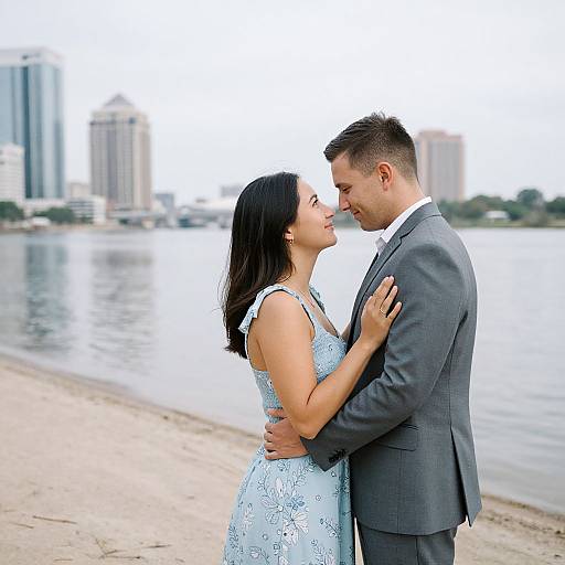 Photograph of a couple standing on a beach, facing each other, the woman in a light blue floral dress and the man in a gray suit,