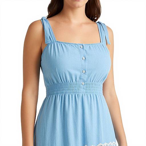 Photograph of a woman wearing a light blue, sleeveless sundress with white buttons, standing against a plain white background.