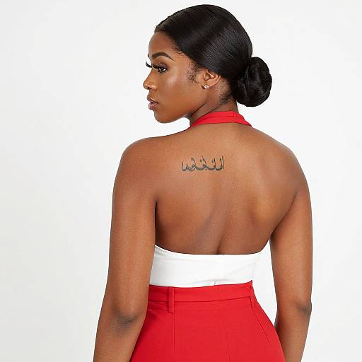 Photograph of a dark-skinned woman with black hair in a bun, wearing a red and white halter-top dress, showing a tattoo on her