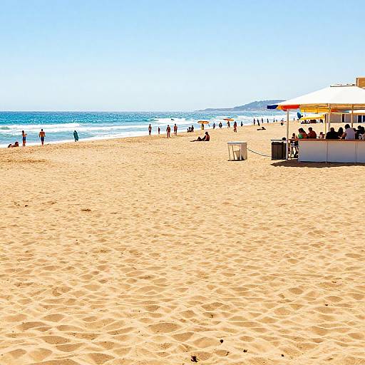 Bright photograph of a sandy beach with scattered people, colorful umbrellas, and clear blue ocean under a cloudless sky.