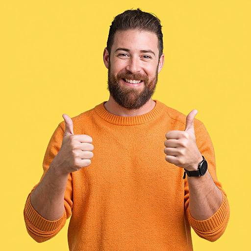 Photograph of a bearded man with short dark hair, smiling, wearing an orange sweater, giving two thumbs up against a bright yellow background.