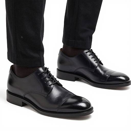 Photograph of a pair of sleek, black leather dress shoes with laces, worn with black dress pants and dark socks.