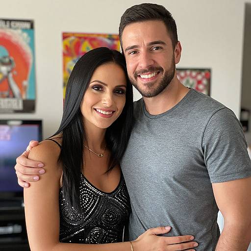 Photograph of a smiling couple; woman with long black hair, sparkly black dress, man with short brown hair, grey t-shirt, in brightly