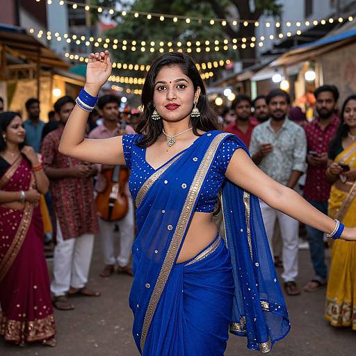 Photograph of a confident Indian woman in a blue, gold-embellished saree, dancing in a lively street festival with string lights and spectators
