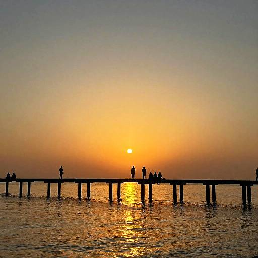 Photograph of a serene sunset over a silhouetted wooden pier, with small figures standing along the edge, reflecting golden sunlight on calm water.