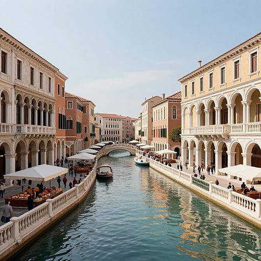 Photograph of a sunlit Venetian canal with arched buildings, outdoor cafes, white umbrellas, gondolas, and a small bridge