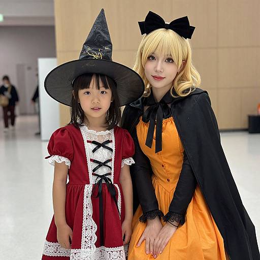 Photograph of an Asian woman and young girl in Halloween costumes; woman in orange dress and black cape, girl in red lace dress and witch hat,