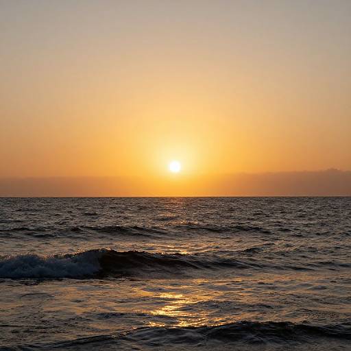 Photograph of a serene ocean sunset, with the golden sun setting on the horizon, casting a warm orange glow over gentle, dark blue waves.