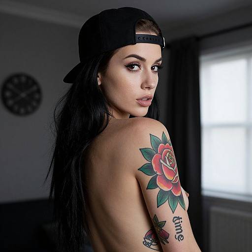 Photograph of a topless woman with long black hair, wearing a backward black cap, showcasing a colorful rose tattoo on her right shoulder, in a