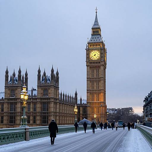 Photograph of the snow-covered Westminster Bridge at dusk, featuring the illuminated Big Ben clock tower and Gothic Parliament buildings, with people walking in winter coats.