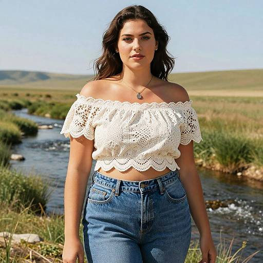 Photograph of a young woman with long dark hair, wearing a white off-shoulder lace top and high-waisted blue jeans, standing by