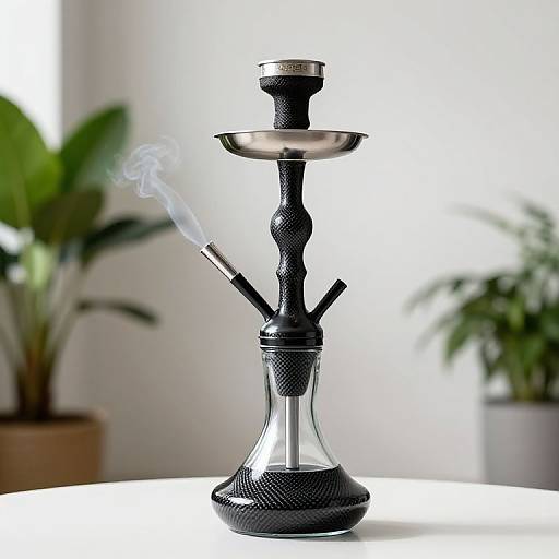 Photograph of a sleek, black and silver hookah with a smoking pipe, standing on a white table, with two blurred green plants in the background