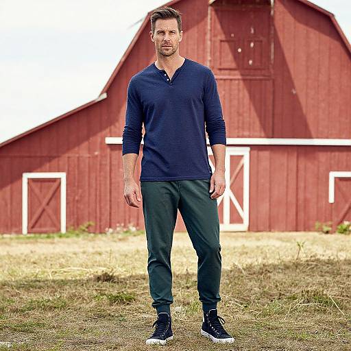 Photograph of a handsome man with short brown hair, wearing a navy long-sleeve henley, dark pants, and black sneakers, standing in