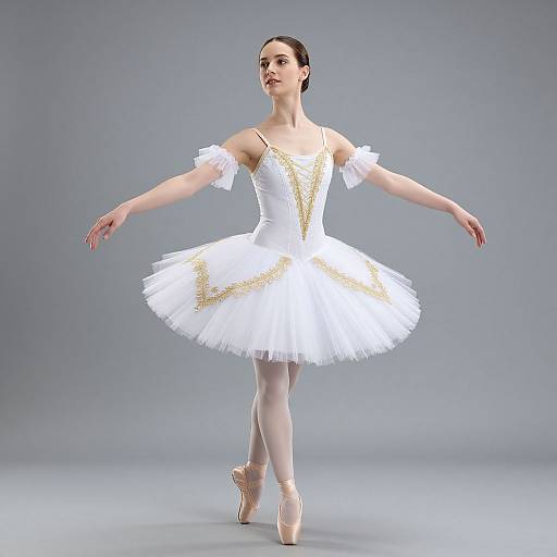 Photograph of a slender, fair-skinned ballerina with dark hair in a bun, wearing a white tutu with gold accents, en point