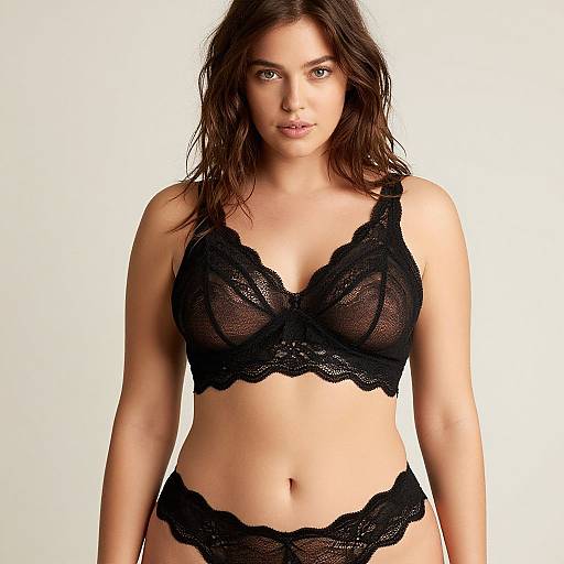 Photograph of a confident, brown-haired woman with fair skin wearing black lace lingerie, featuring a bra and matching panties, against a plain white background.