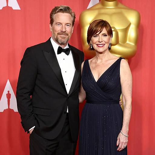 Photograph of a smiling, bearded man in a black tuxedo and a woman with short brown hair in a black, V-neck dress,