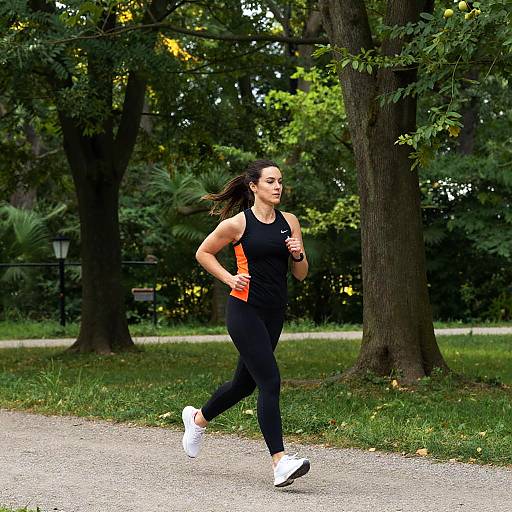 Photograph of a fit woman with long brown hair running in a park, wearing a black tank top, orange accents, black leggings, and white sneakers