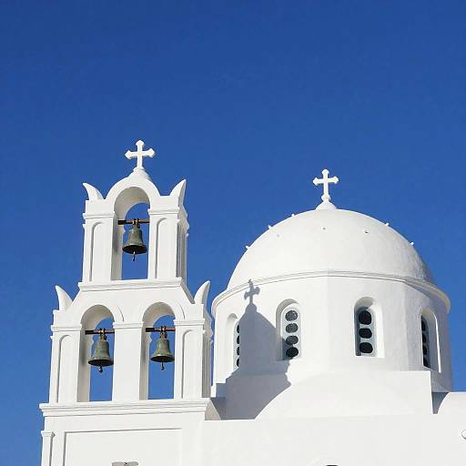 Photograph of a white Greek Orthodox church with bell towers and crosses against a vivid blue sky, highlighting the bright contrast.