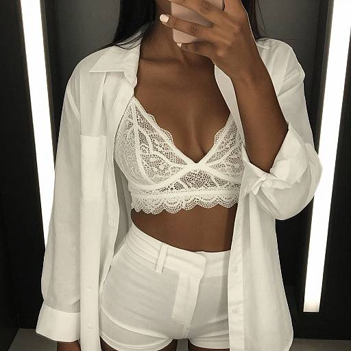 Photograph of a dark-skinned woman with long black hair, wearing an open white shirt, white lace bralette, and high-waisted white