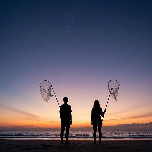 Silhouetted couple holding nets at sunset on a beach, sky gradient from deep blue to orange, serene ocean in background. Photographic image.