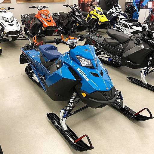 Photograph of a showroom floor displaying various colorful snowmobiles, including a prominent blue one in the foreground, with others in black, white, orange