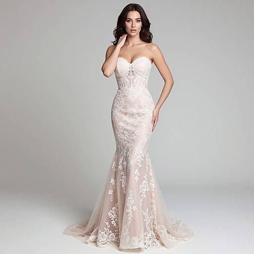 Photograph of a beautiful woman with long dark hair, wearing a strapless, white lace mermaid-style wedding gown, standing against a plain light gray