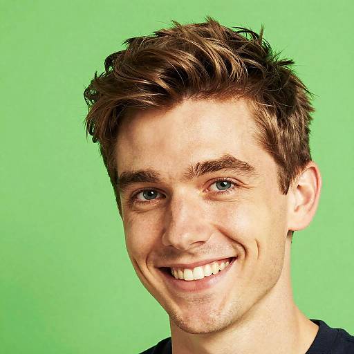 Photograph of a young Caucasian man with short brown hair, blue eyes, and a broad smile against a solid green background.