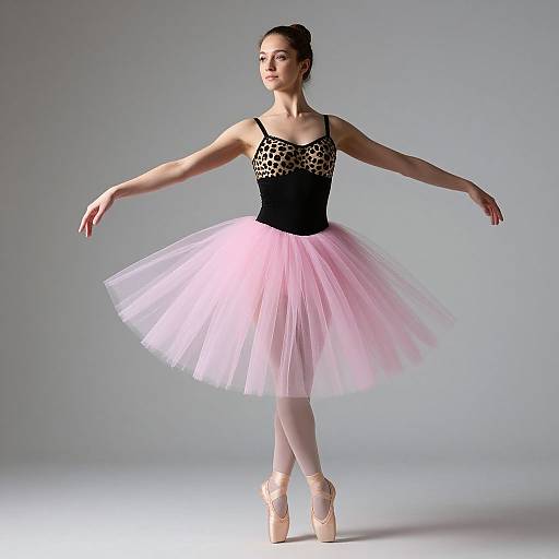 Photograph of a ballerina in a black lace bodice and pink tulle tutu, en pointe, with arms gracefully extended, against